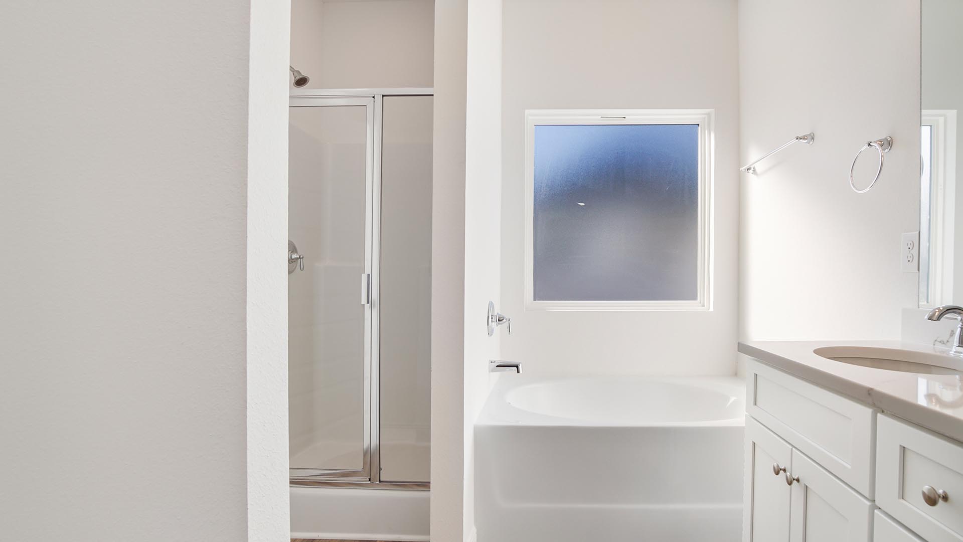 Primary bathroom with double vanity and large soaking tub below frosted glass window and separate standing shower.