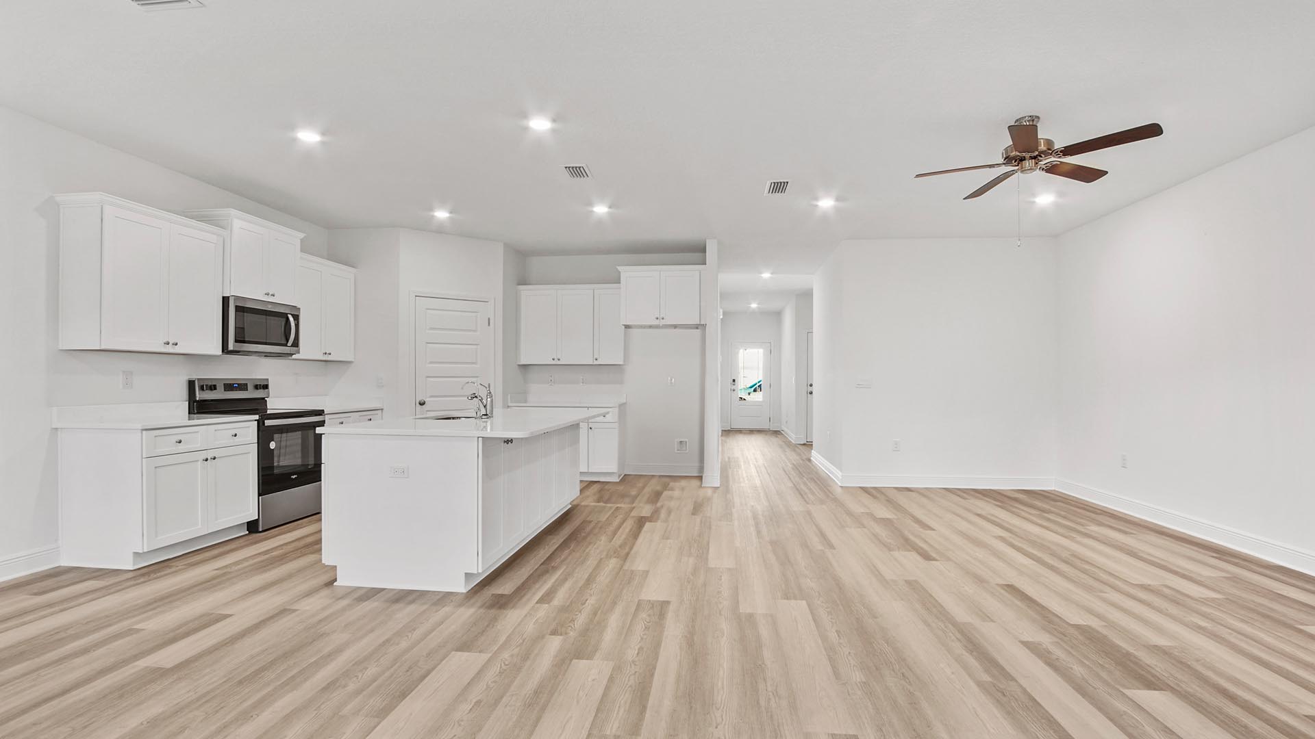 Kitchen island overlooking living area with EVP flooring and ceiling fan and hallway to foyer.
