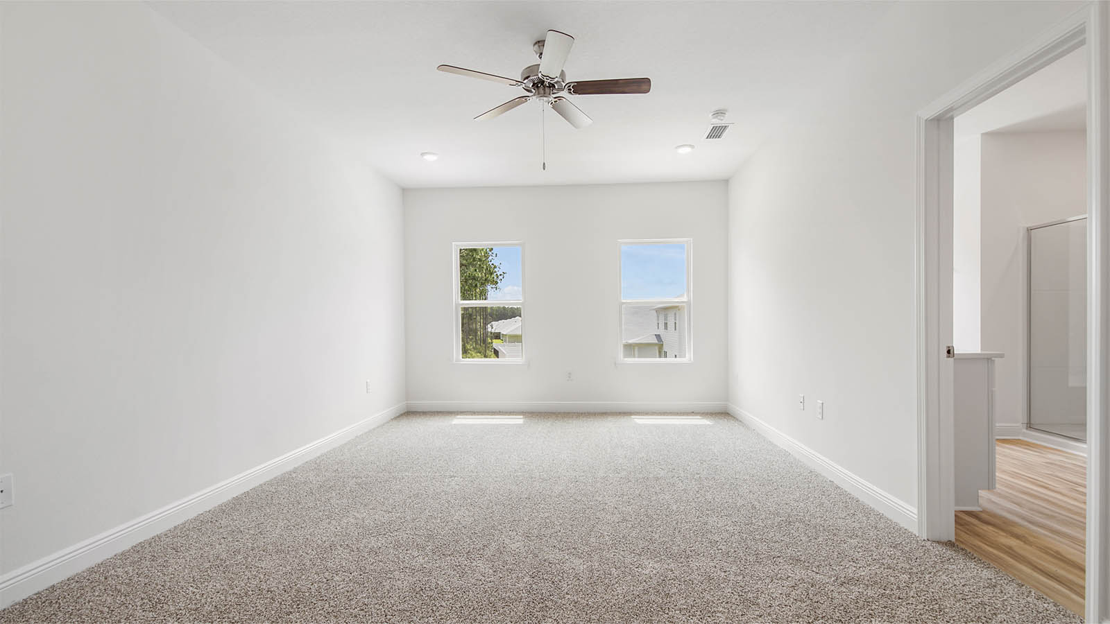 Primary bedroom with carpet and two windows and ceiling fan.