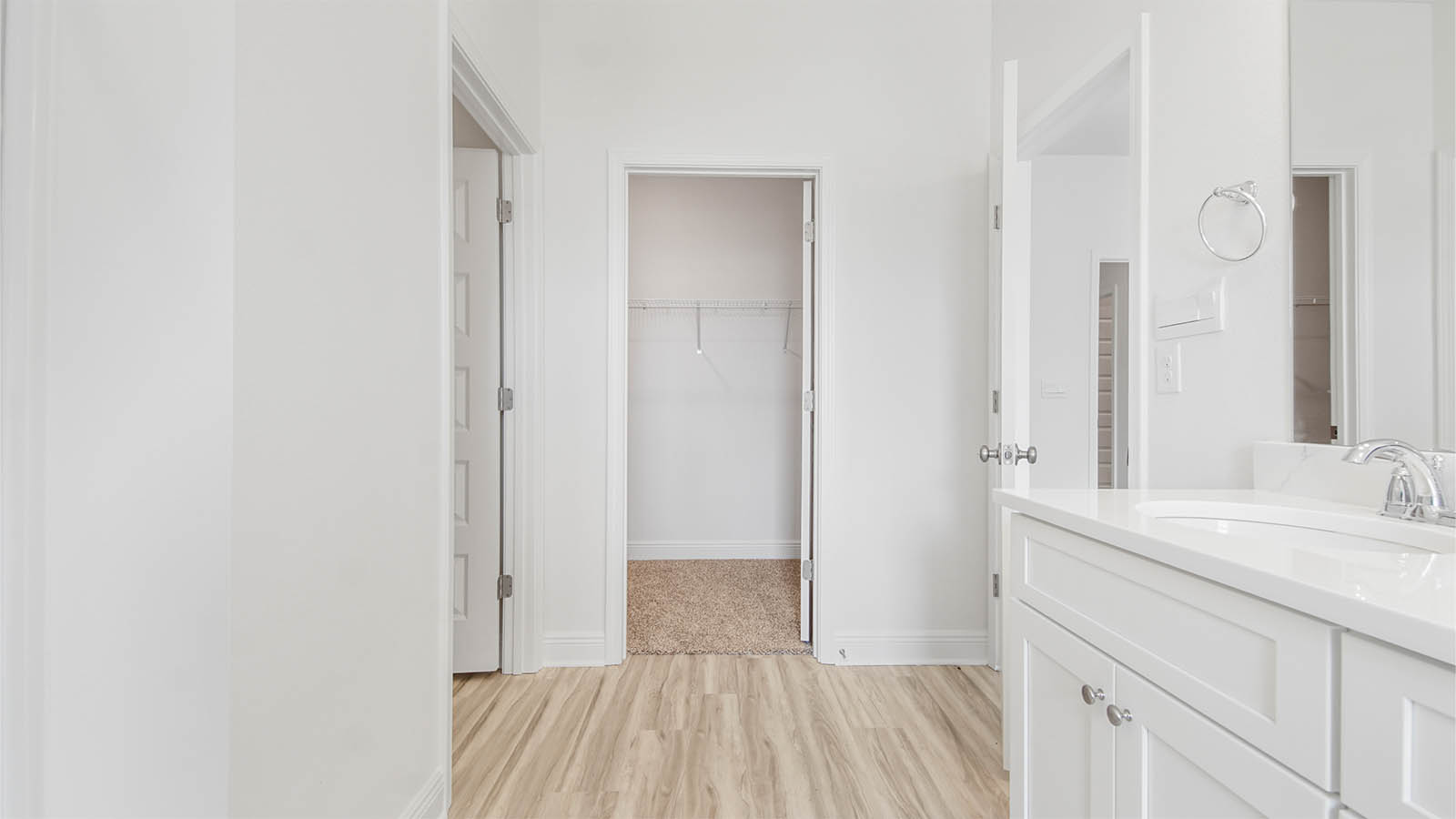 Primary bathroom with EVP flooring and walk-in closet and double sink vanity with quartz countertops and white cabinetry.