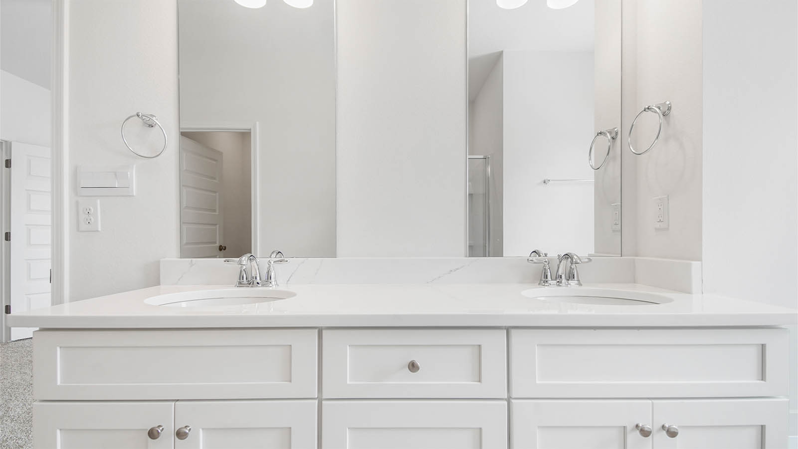 Primary bathroom with double sink vanity and quartz countertops and white cabinetry.
