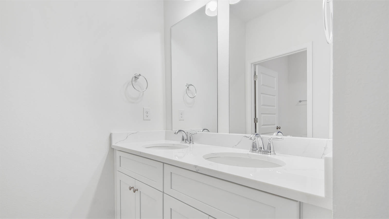 Bathroom three with double vanity with quartz countertops and white cabinetry across from shower room entrance.