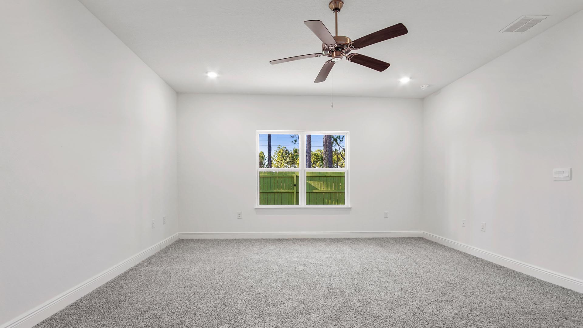 Primary bedroom with a large window and ceiling fan and carpet flooring.