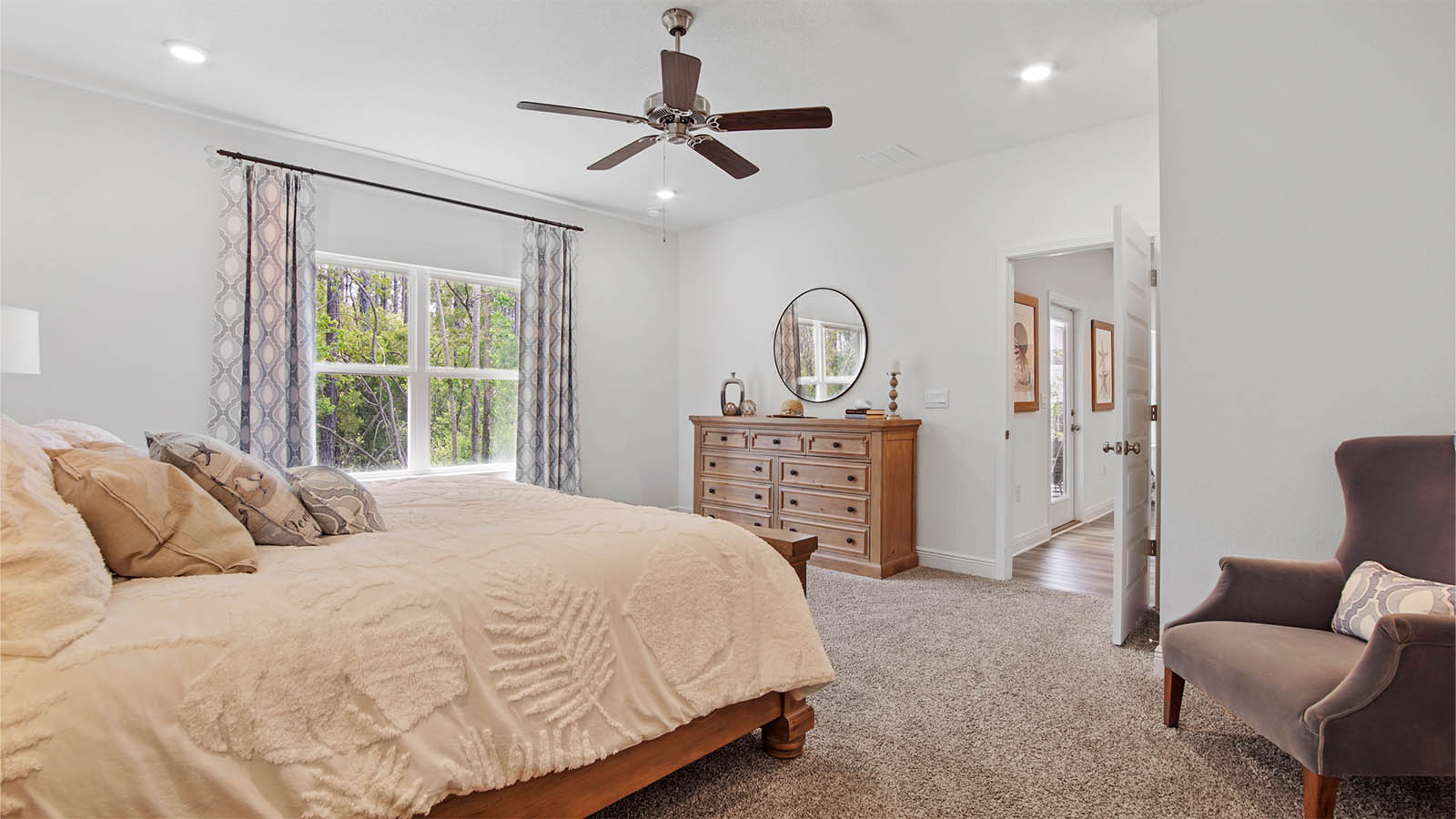 Primary bedroom with large window and ceiling fan and carpet flooring.