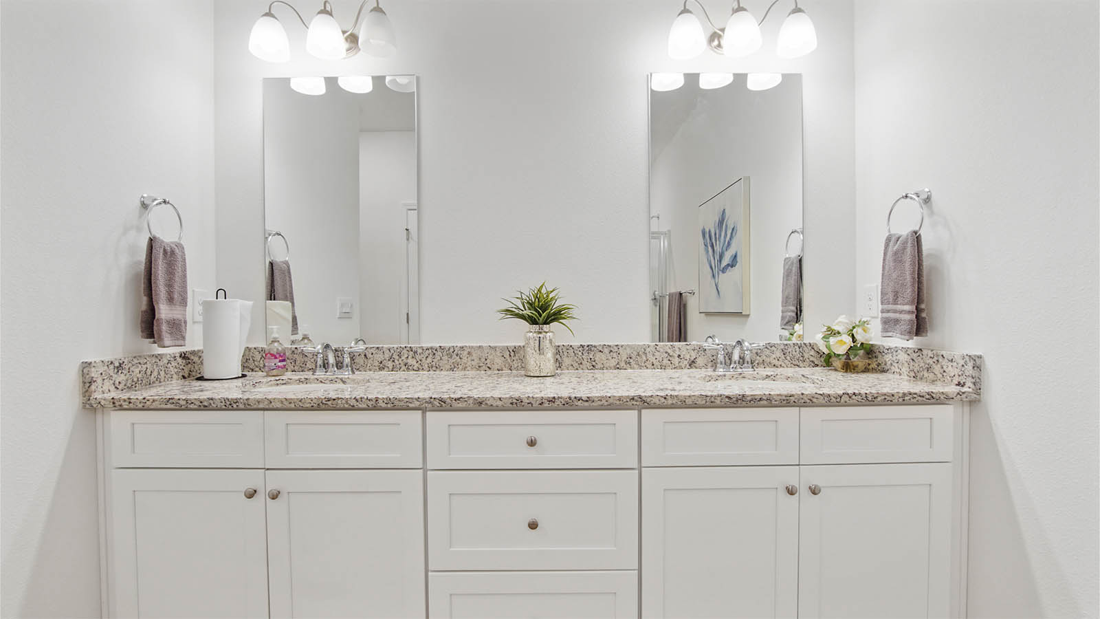 Primary bathroom with double vanity with white cabinetry and granite countertops.