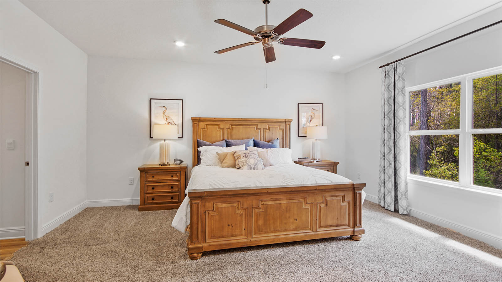 Primary bedroom with a large window and ceiling fan and carpet flooring.