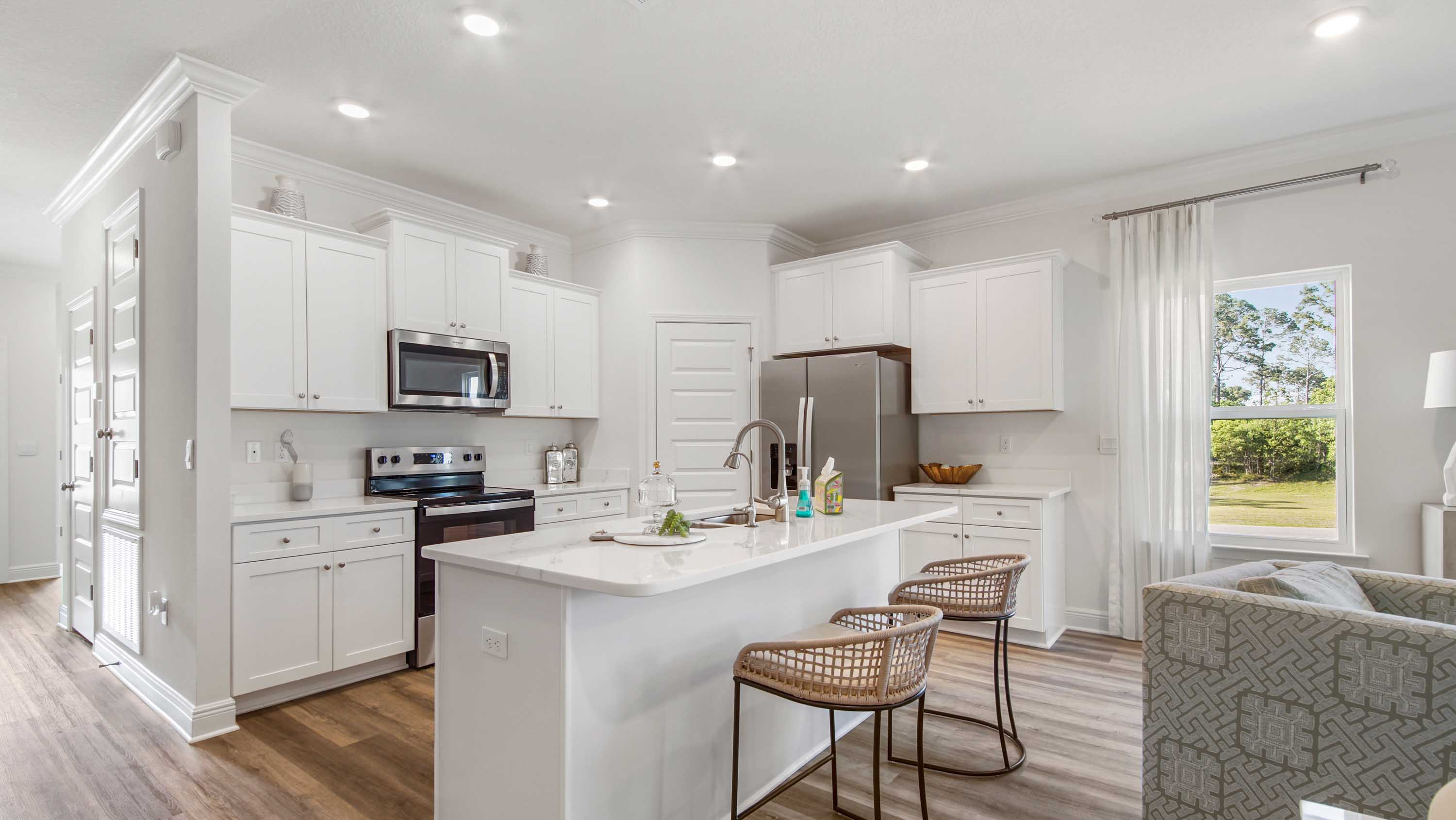 Kitchen with EVP flooring and quartz countertops and white cabinetry next to living area with windows.