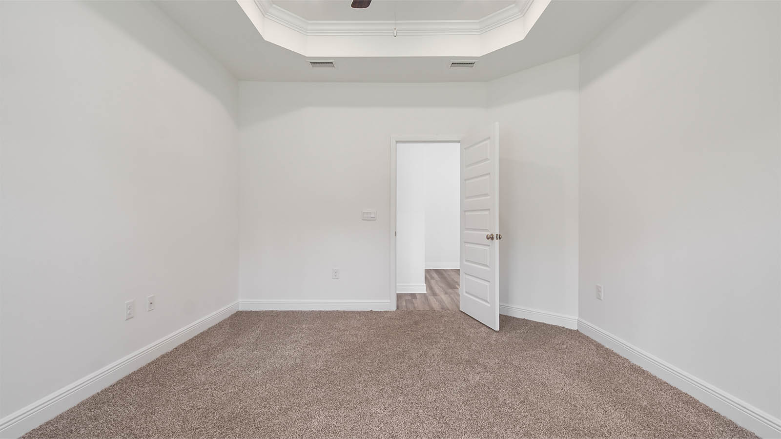 Primary bedroom with tray ceilings and ceiling fan and carpet flooring.