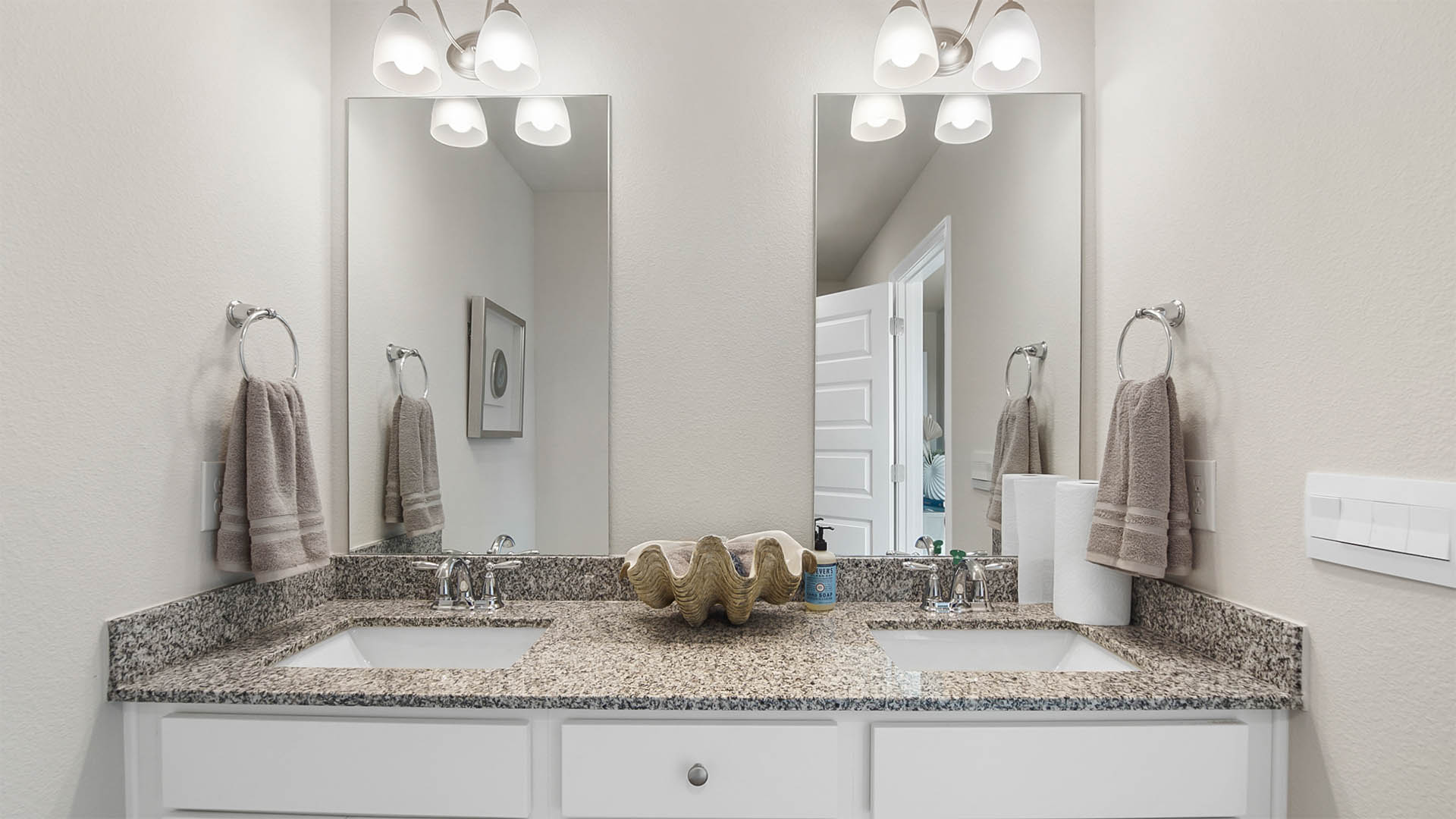 Primary bathroom with double sink vanity and granite counter tops and white cabinetry and two mirrows.