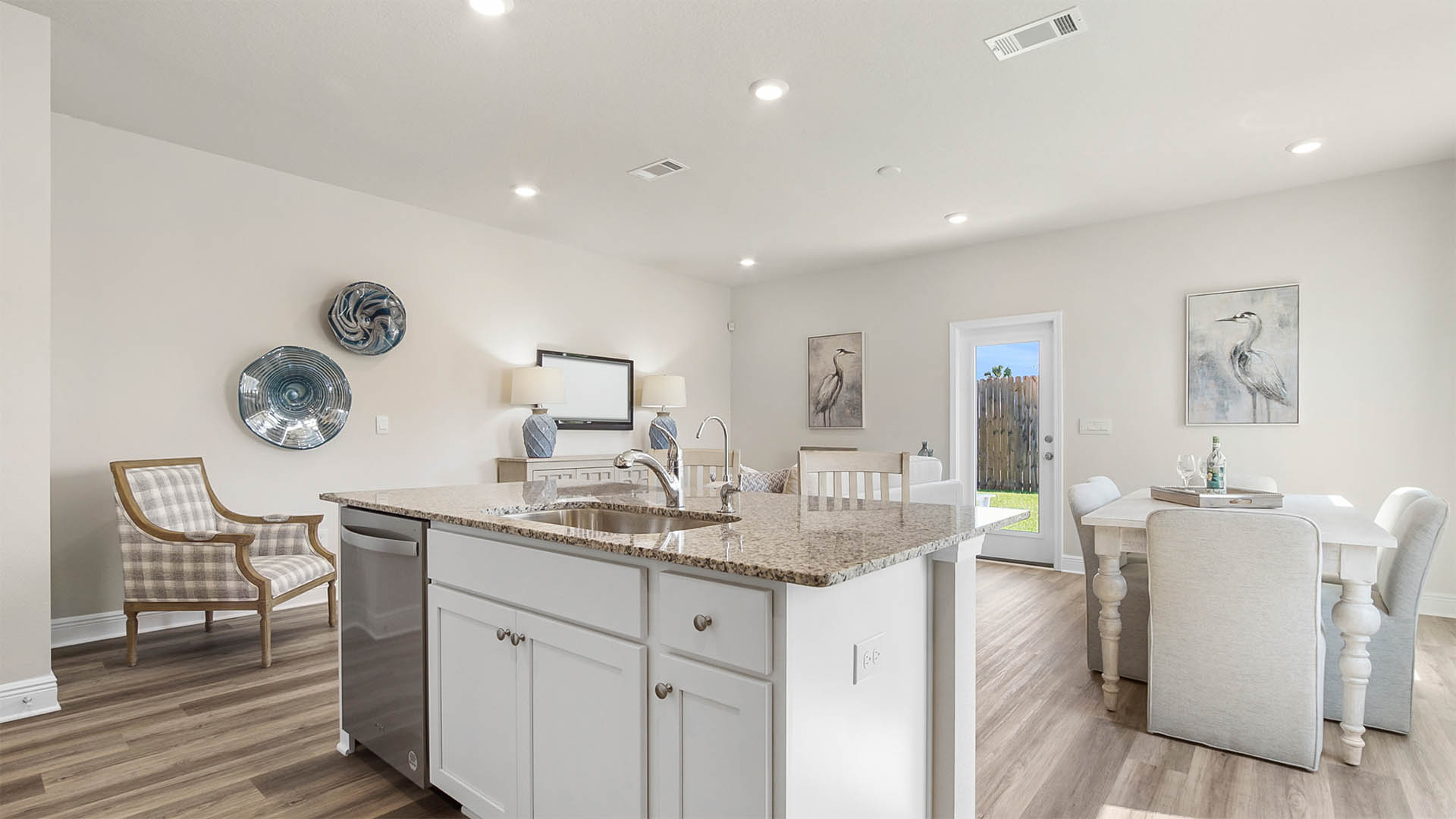 Kitchen island with granite countertops and white cabinetry and under mount kitchen sink and dishwasher in island.