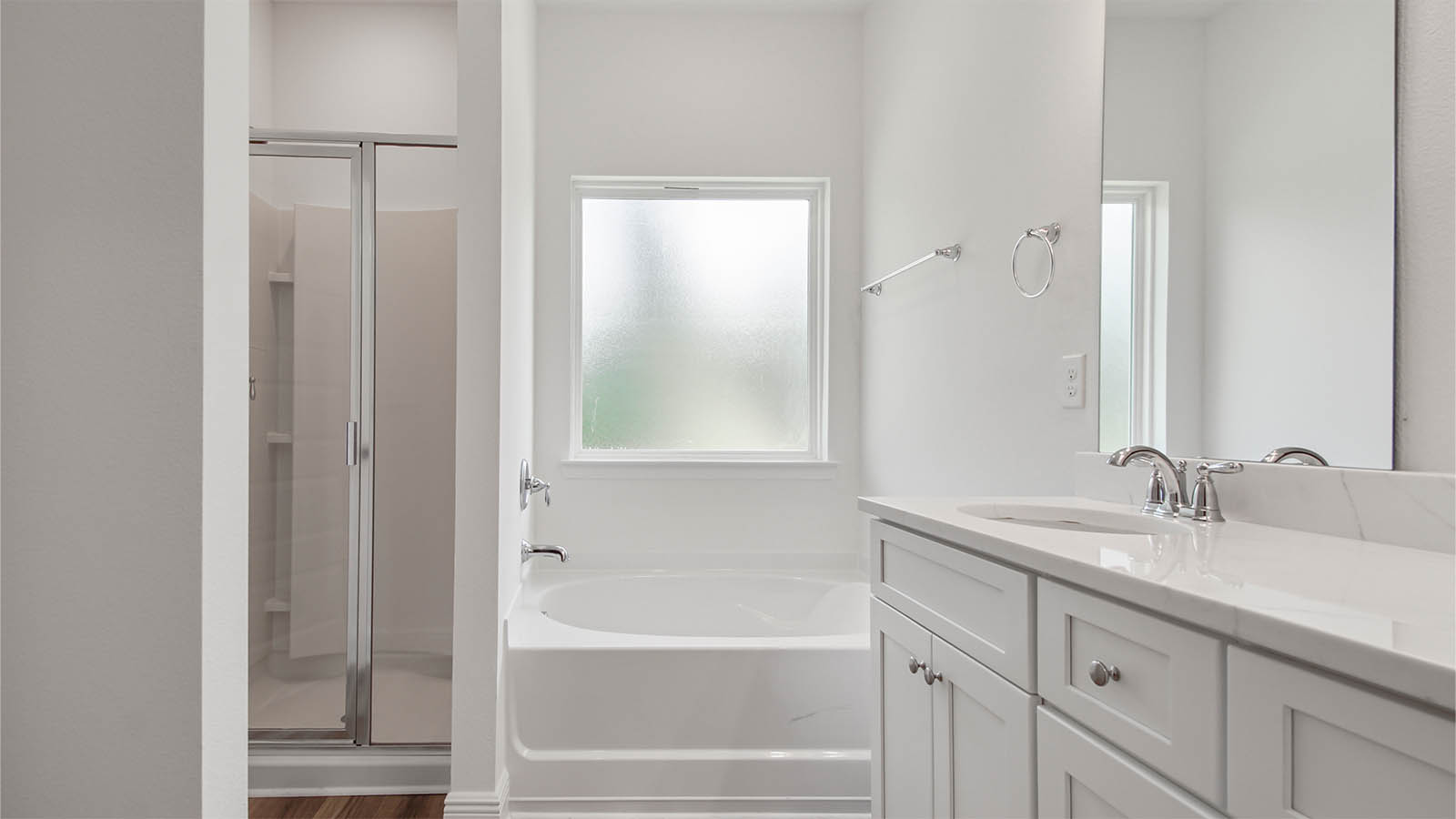 Primary bathroom with double vanity and large soaking tub below frosted glass window and separate standing shower.