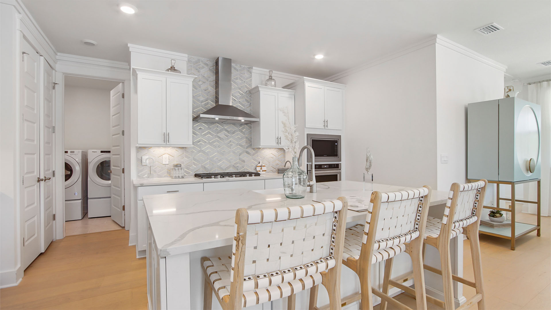 Open kitchen with large island and wood flooring and quarts countertops and white cabinetry and gas stove.