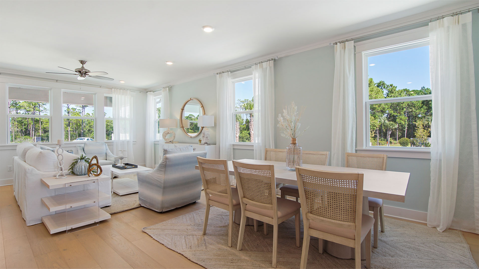 Dining room next to living area with windows and wood flooring.