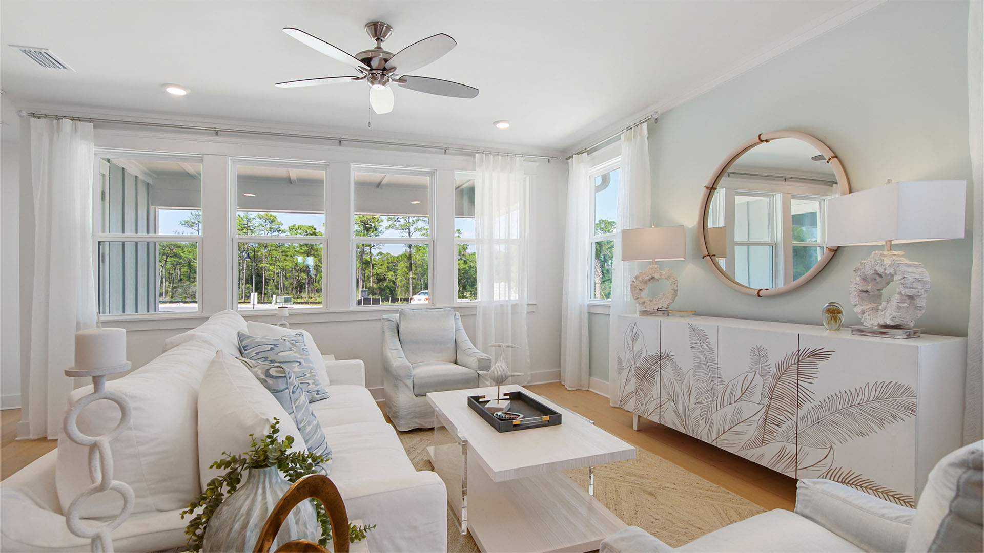 Living room with wood flooring and windows looking out to covered back patio.