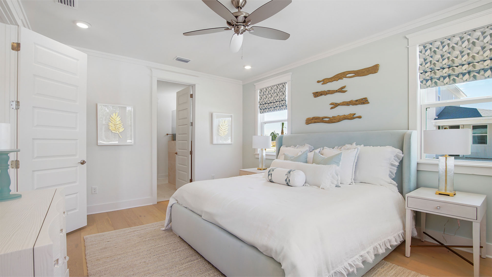 Primary bedroom with windows and wood flooring and ceiling fan and primary bathroom entrance.