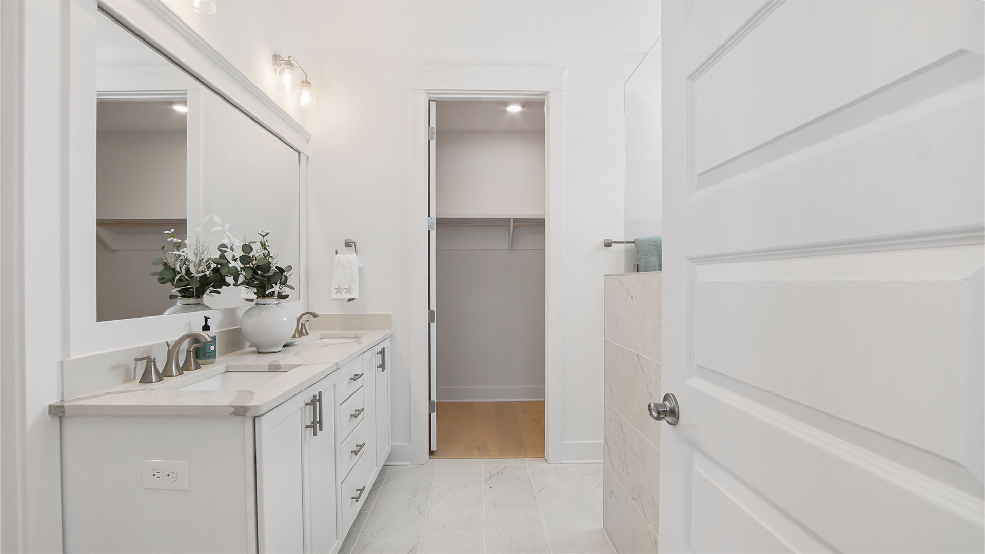 Primary bathroom with tile flooring and two sink vanity and quarts countertops and white cabinetry and walk-in closet.
