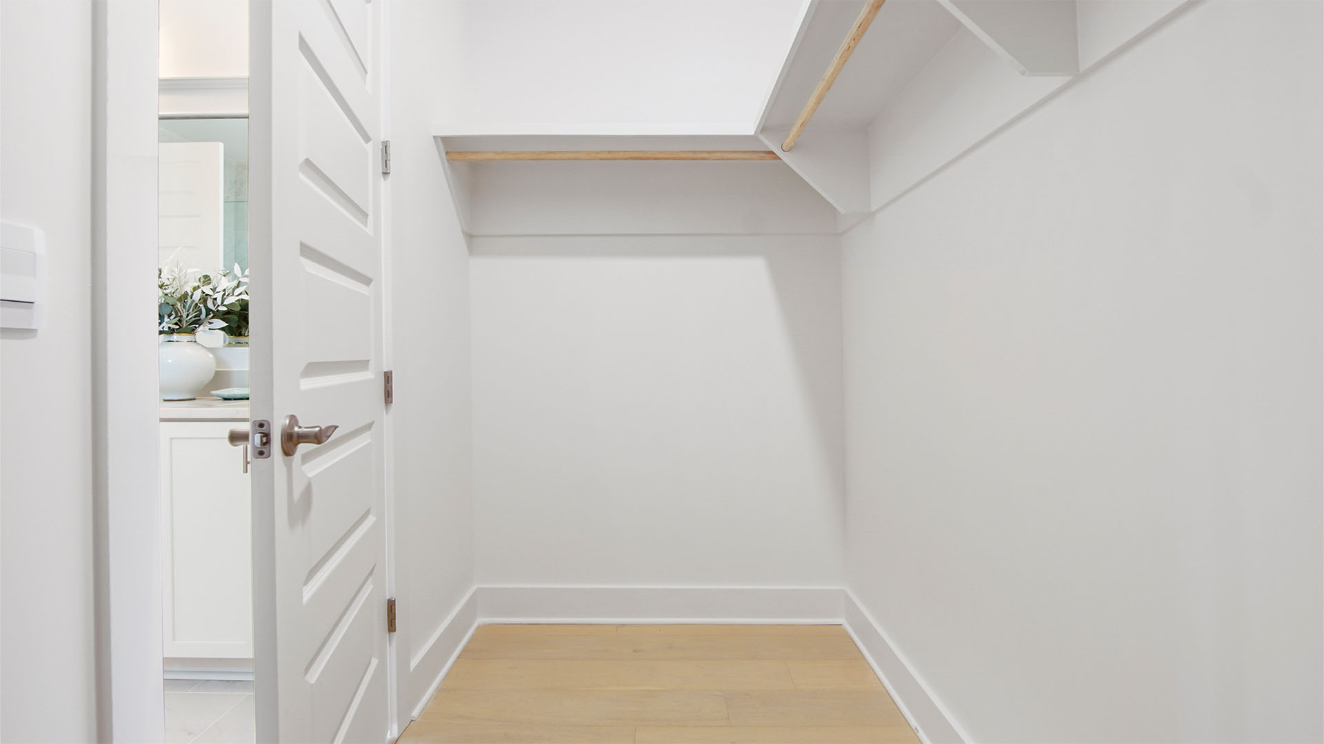 Walk-in primary closet with wood flooring and wood shelving.