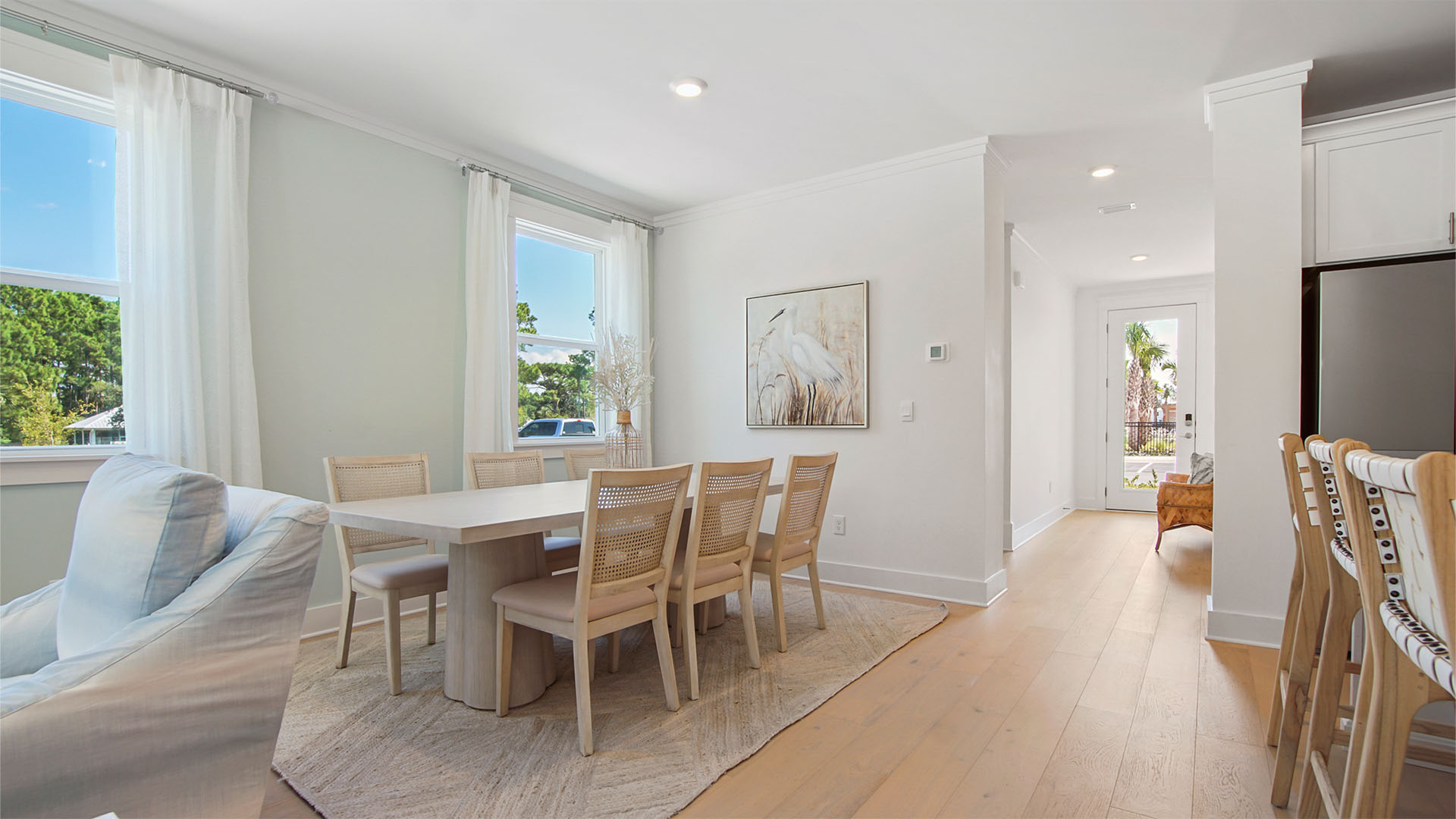 Dining room with wood flooring next to hallway to foyer and garage entrance and stairs.