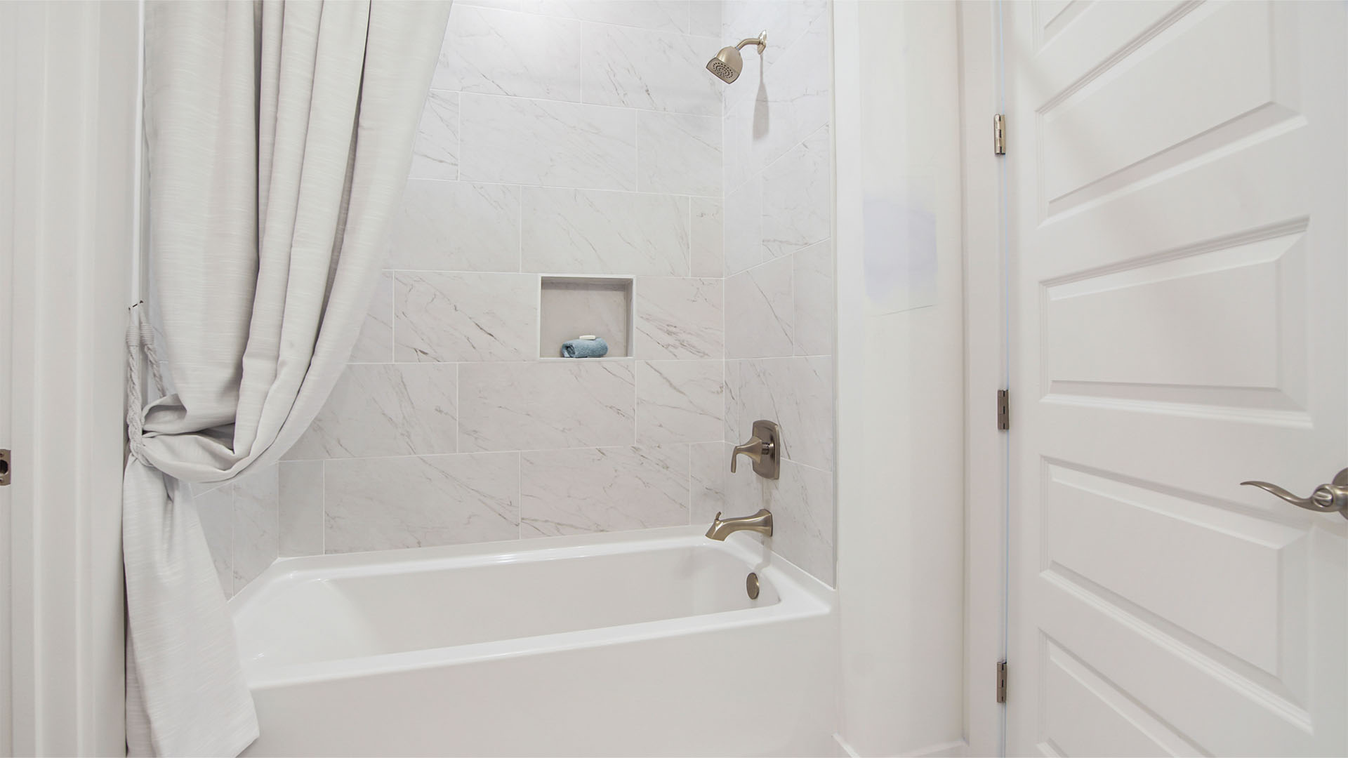 Tub shower with tile walls and wall cutout shelf.