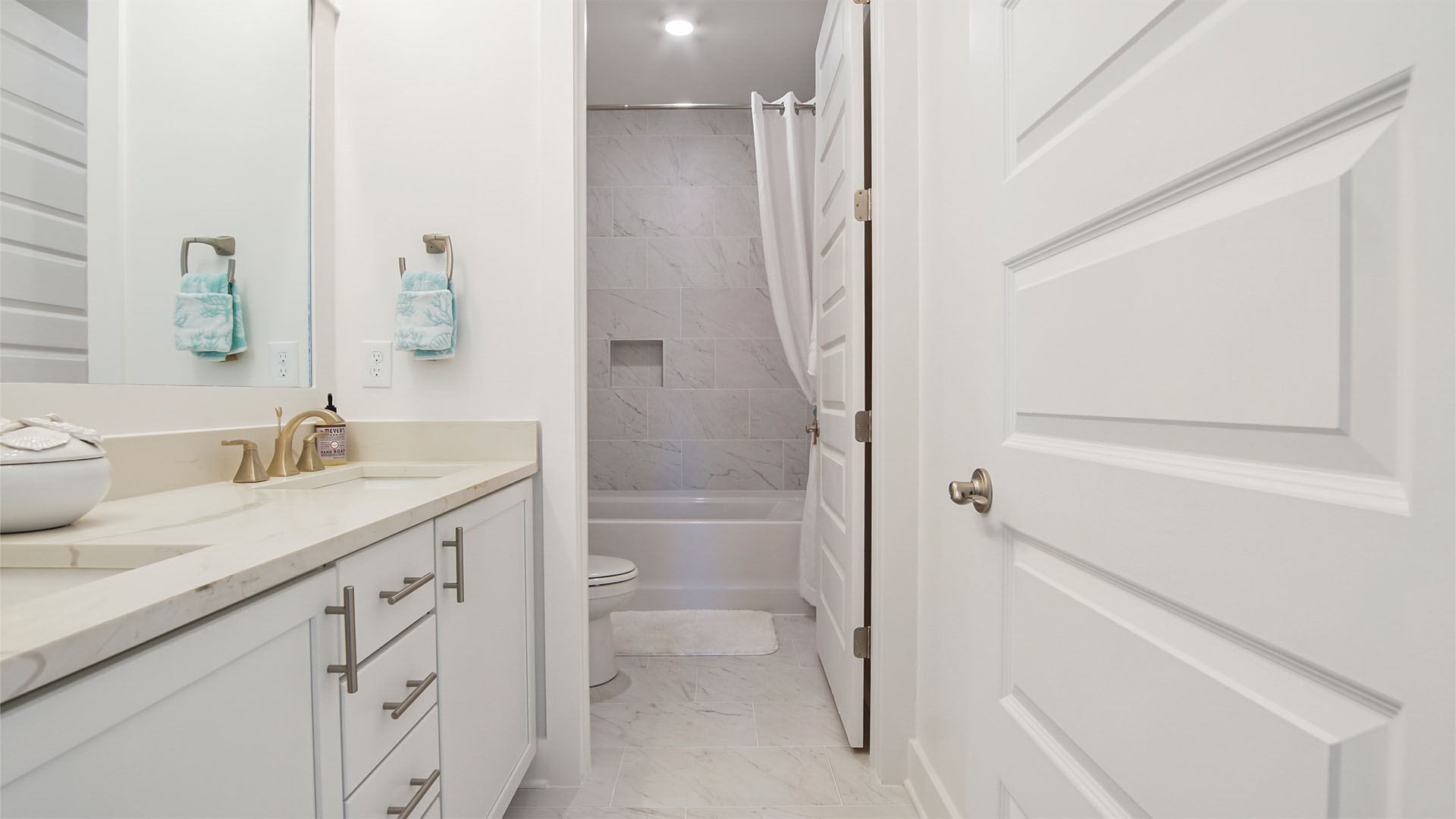 Full bathroom with two sink vanity with quartz countertops and white cabinetry and door to shower room with toilet.