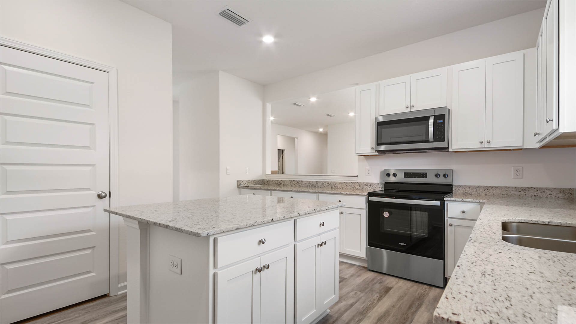 Kitchen island with lower cabinetry and drawers for storage. White cabinetry surrounding and service window from kitchen to dining area