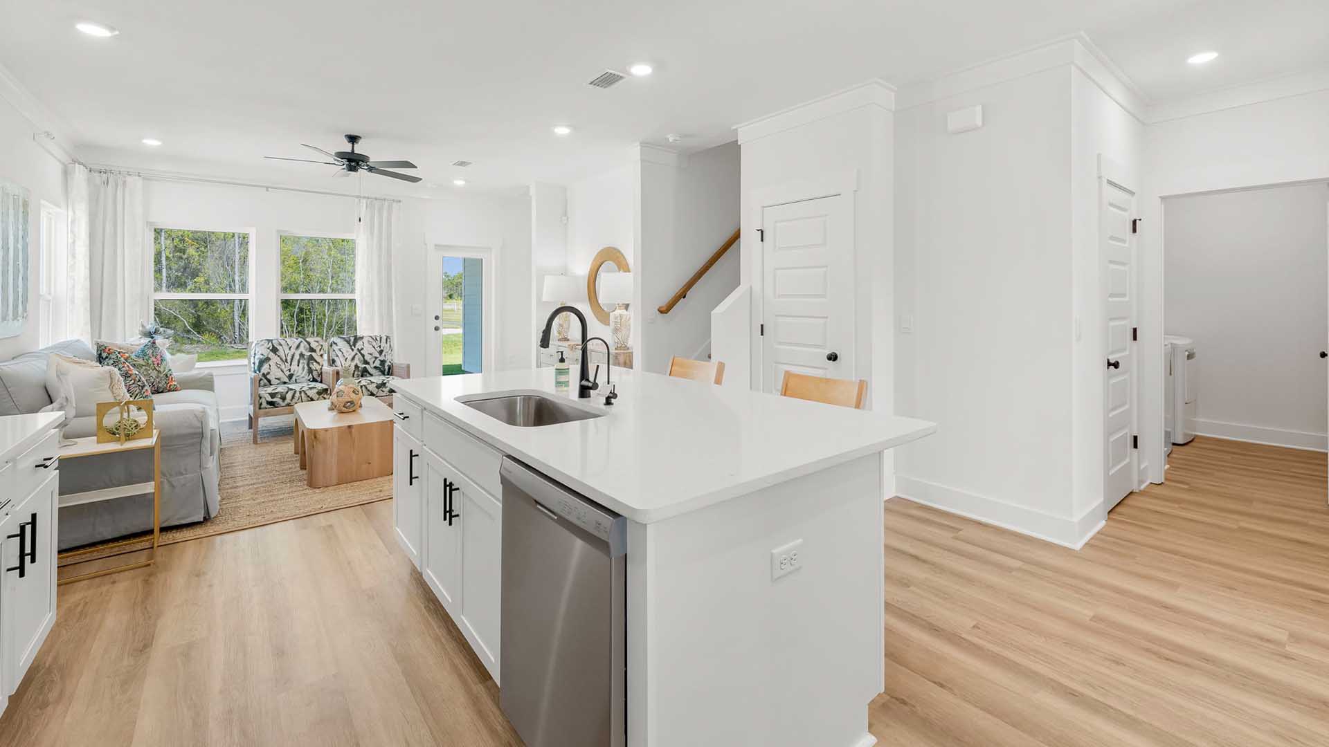 The kitchen has an island with sink and dishwasher and looks out to the living area and stairs