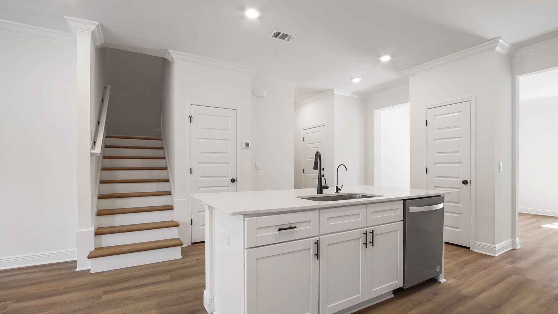 The kitchen has an island with sink and dishwasher and looks out to the living area and stairs