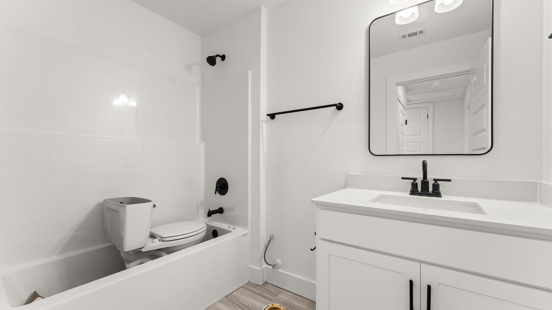 The shared bathroom has a single vanity with matte black fixtures, quartz countertops and a shower tub combination