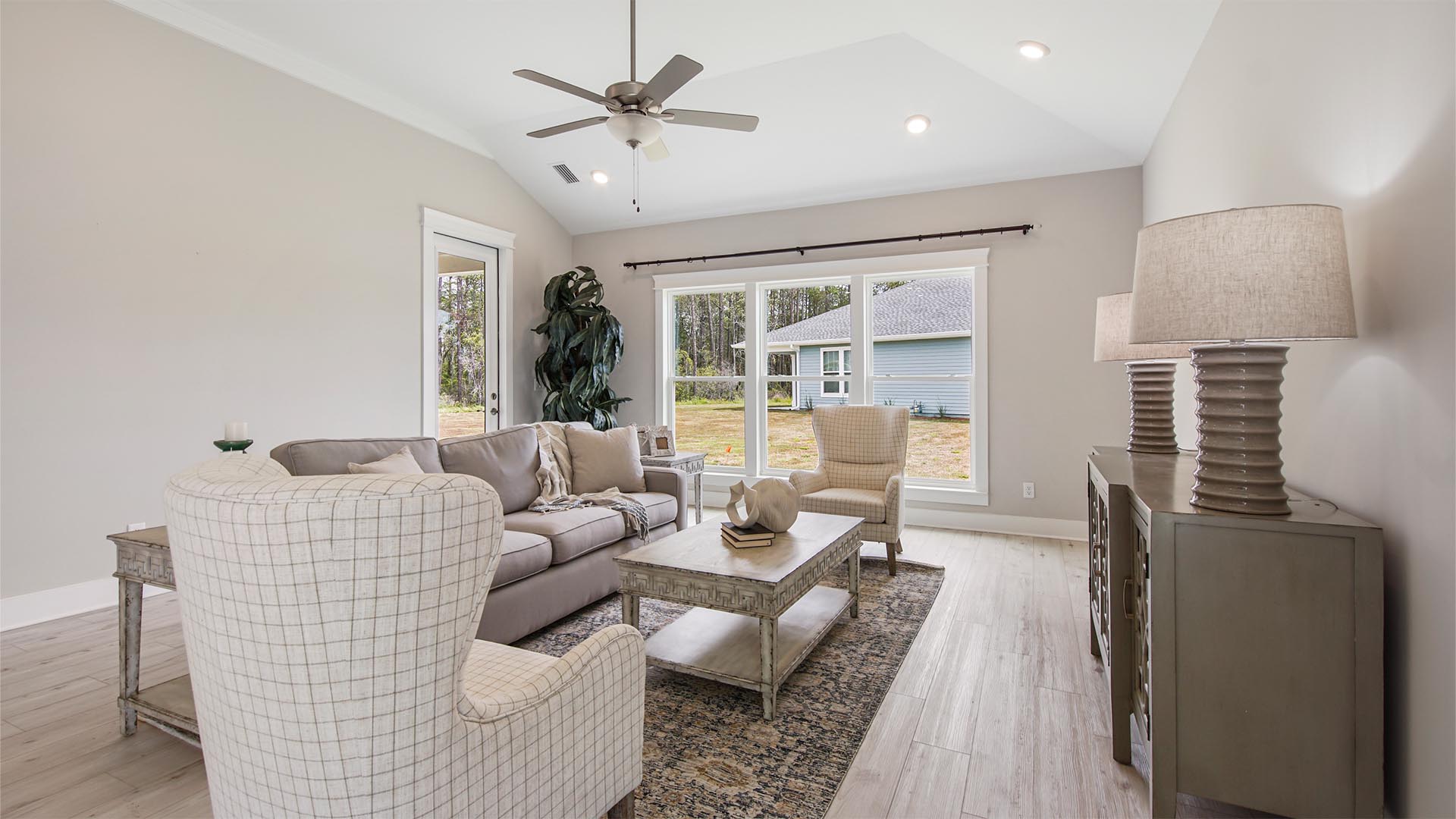 Bright living area with large windows and EVP flooring and ceiling fan and hallway to primary bedroom.