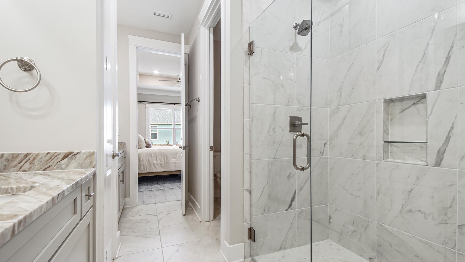 Primary bathroom with oversized tile shower with glass door and water closet and tile flooring and dual vanities.