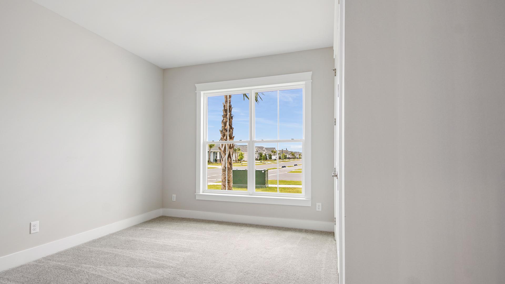 Bedroom two with large picture window facing out the front of the home with carpet flooring.