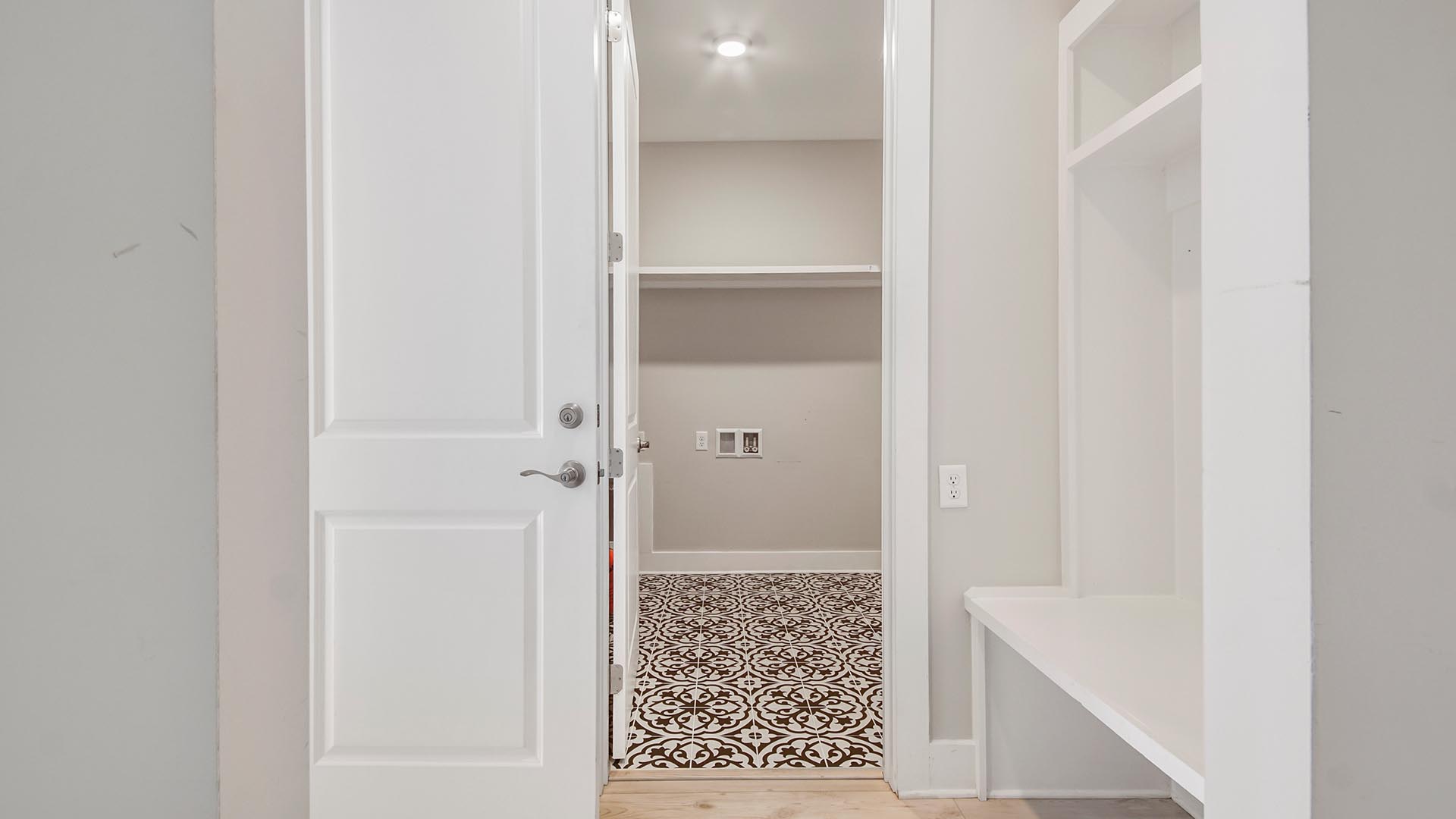 Mudroom across from door to garage and next to laundry room with accent floor and wood shelving.