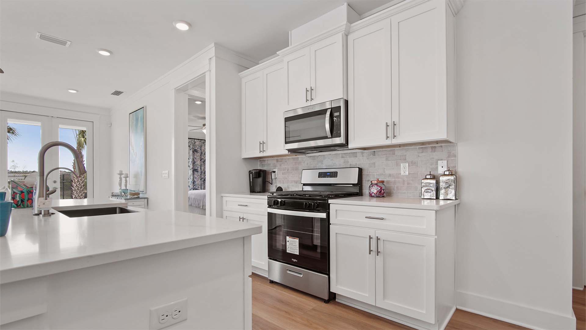 Kitchen with tile backsplash and white cabinetry and quartz countertops and stainless-steel appliances.