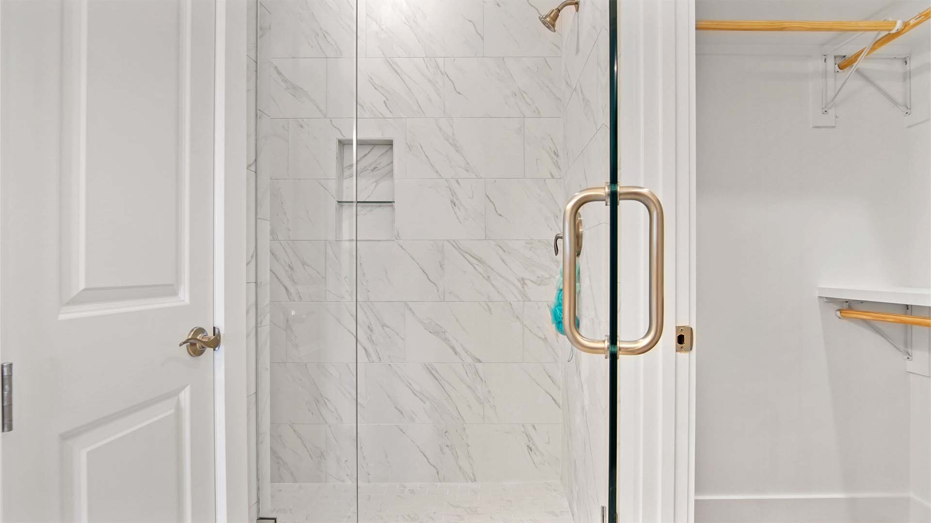 Primary bathroom with oversized tile shower with glass door and walk in closet with wood shelving.