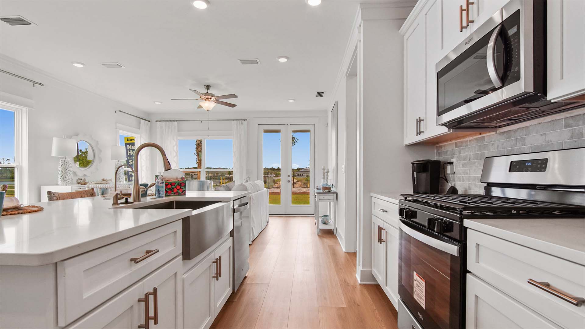 Open concept kitchen with large kitchen island and single basin sink and quarts countertops and white cabinetry.