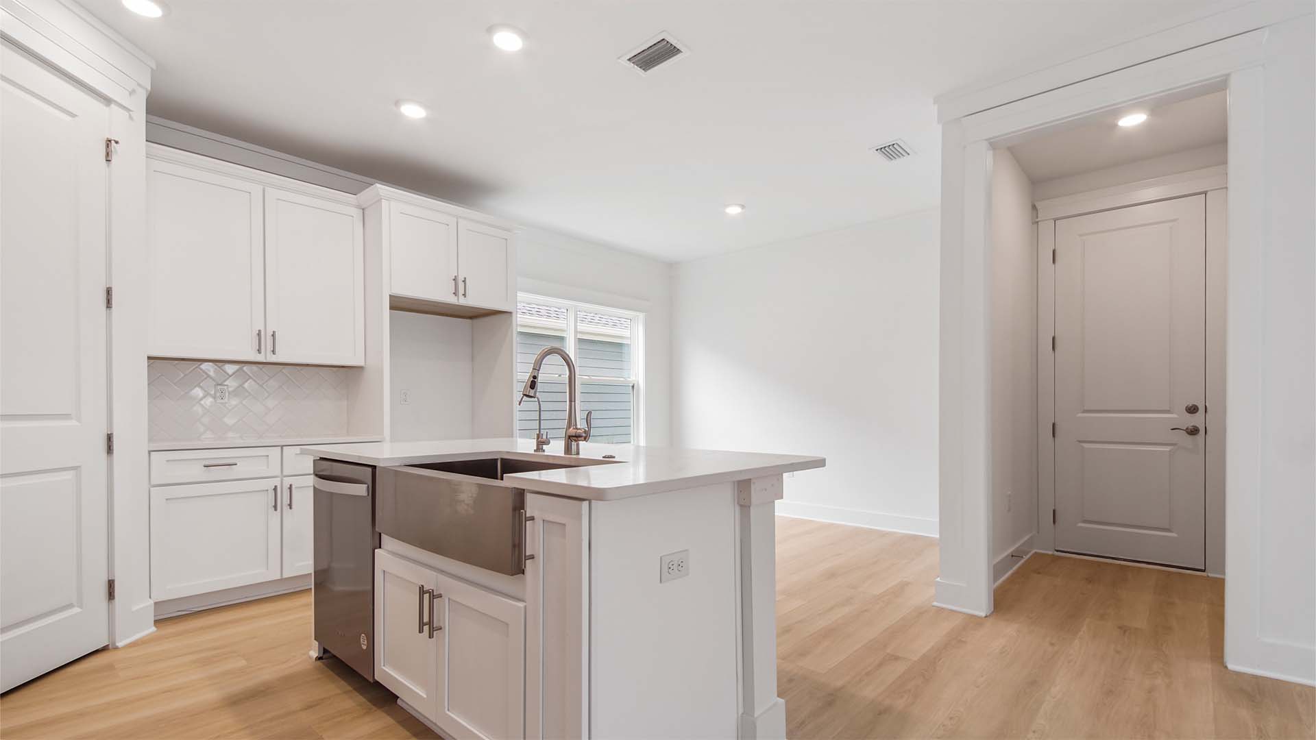 Kitchen and dining area with EVP floor and white cabinetry and quartz countertops and hallway to laundry room and garage.