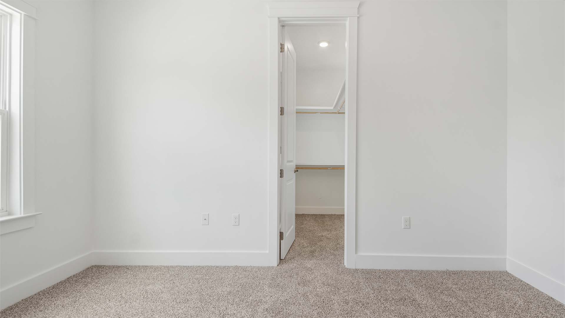 Bedroom five with a large walk-in closet with wood shelving and a window.