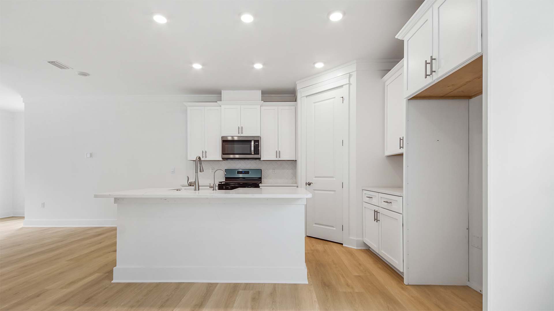 Open kitchen with large island and bar seating and white cabinetry and EVP flooring and quartz countertops and corner pantry.