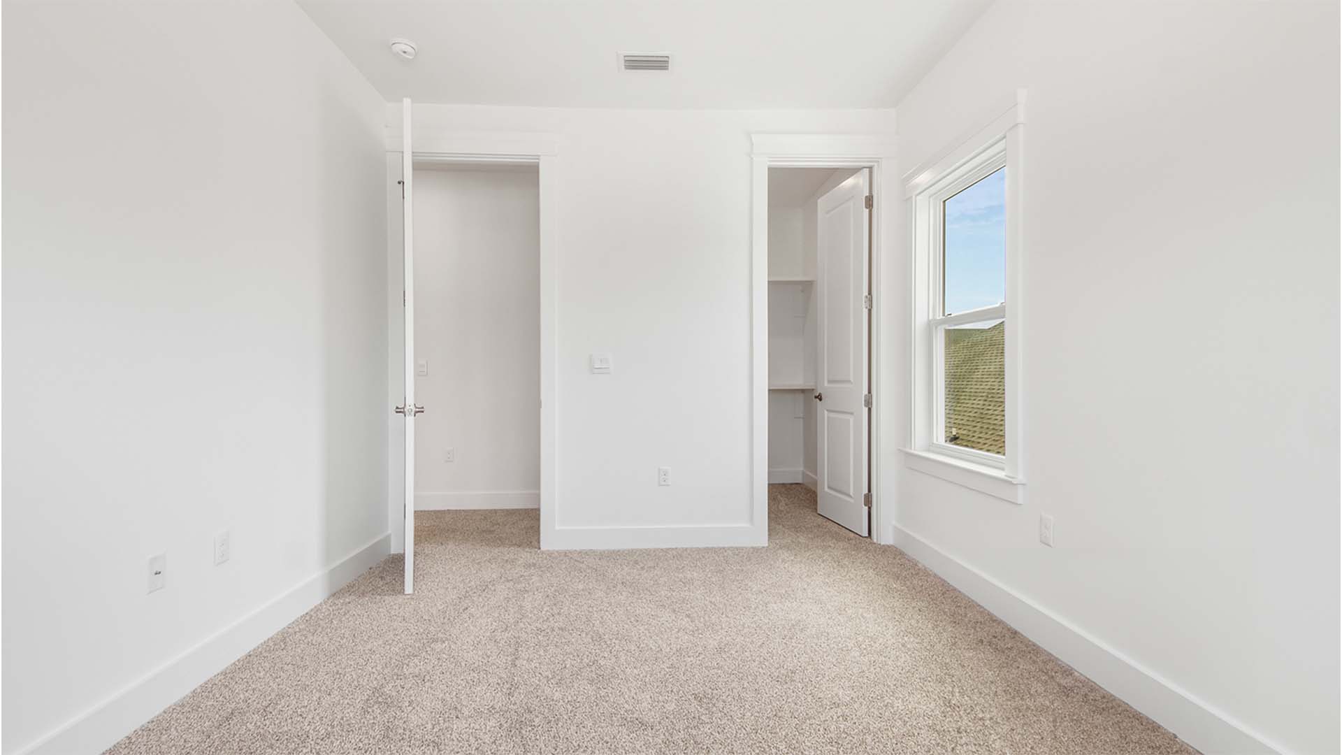 Bedroom four with walk-in closet and large window and carpet flooring.