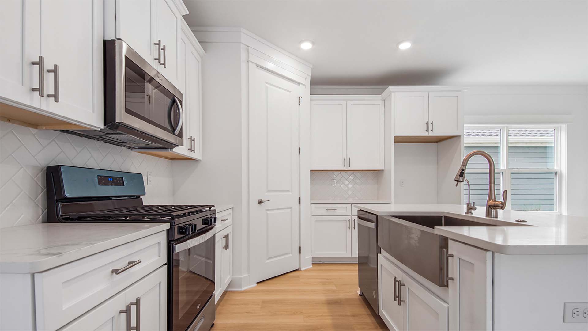 Open concept kitchen with large island with stainless-steel single basin undermount sink and quarts countertops and corner pantry.