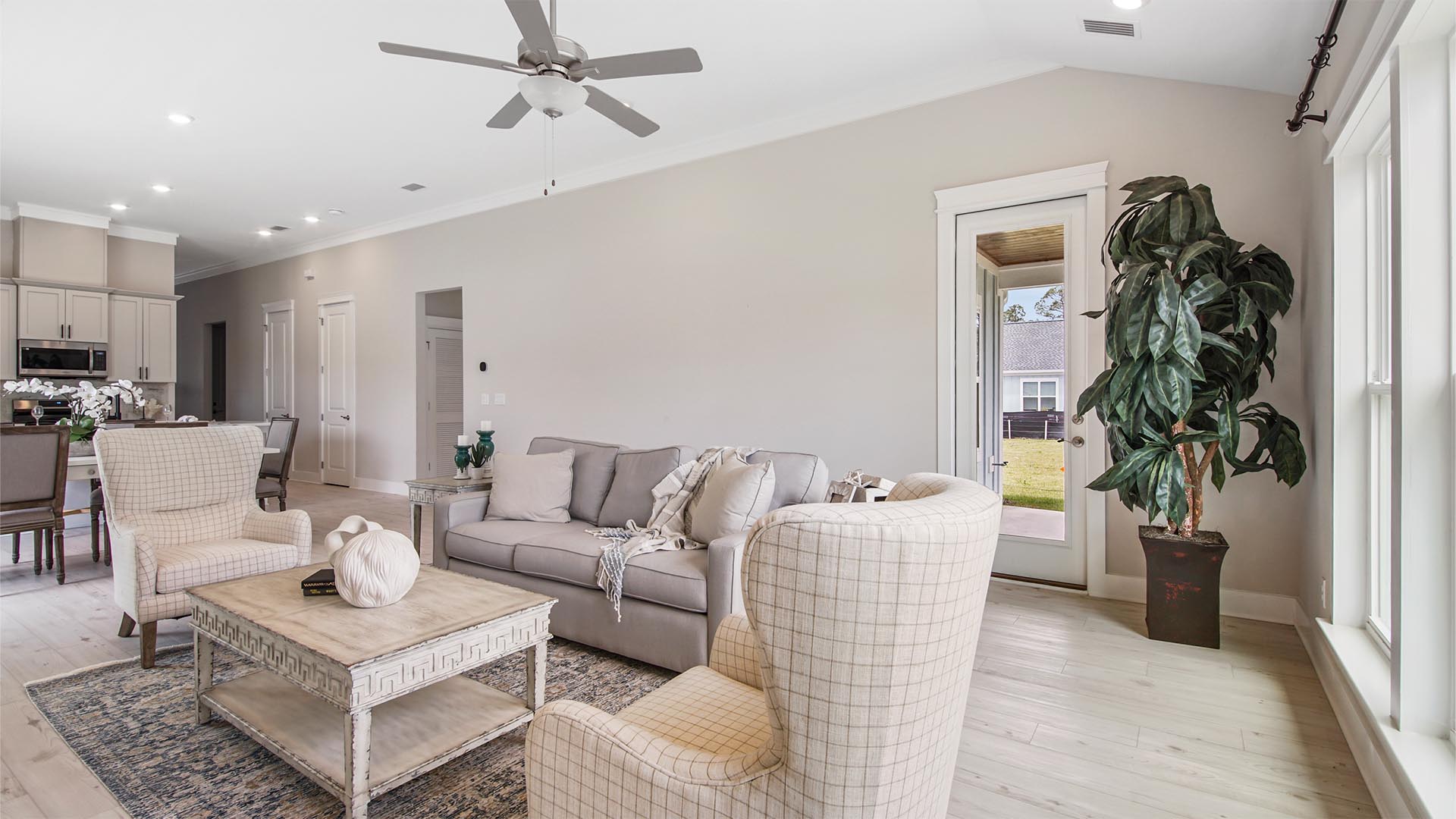 Bright living area with large windows and EVP flooring and vaulted ceilings and ceiling fan and hallway to primary bedroom.