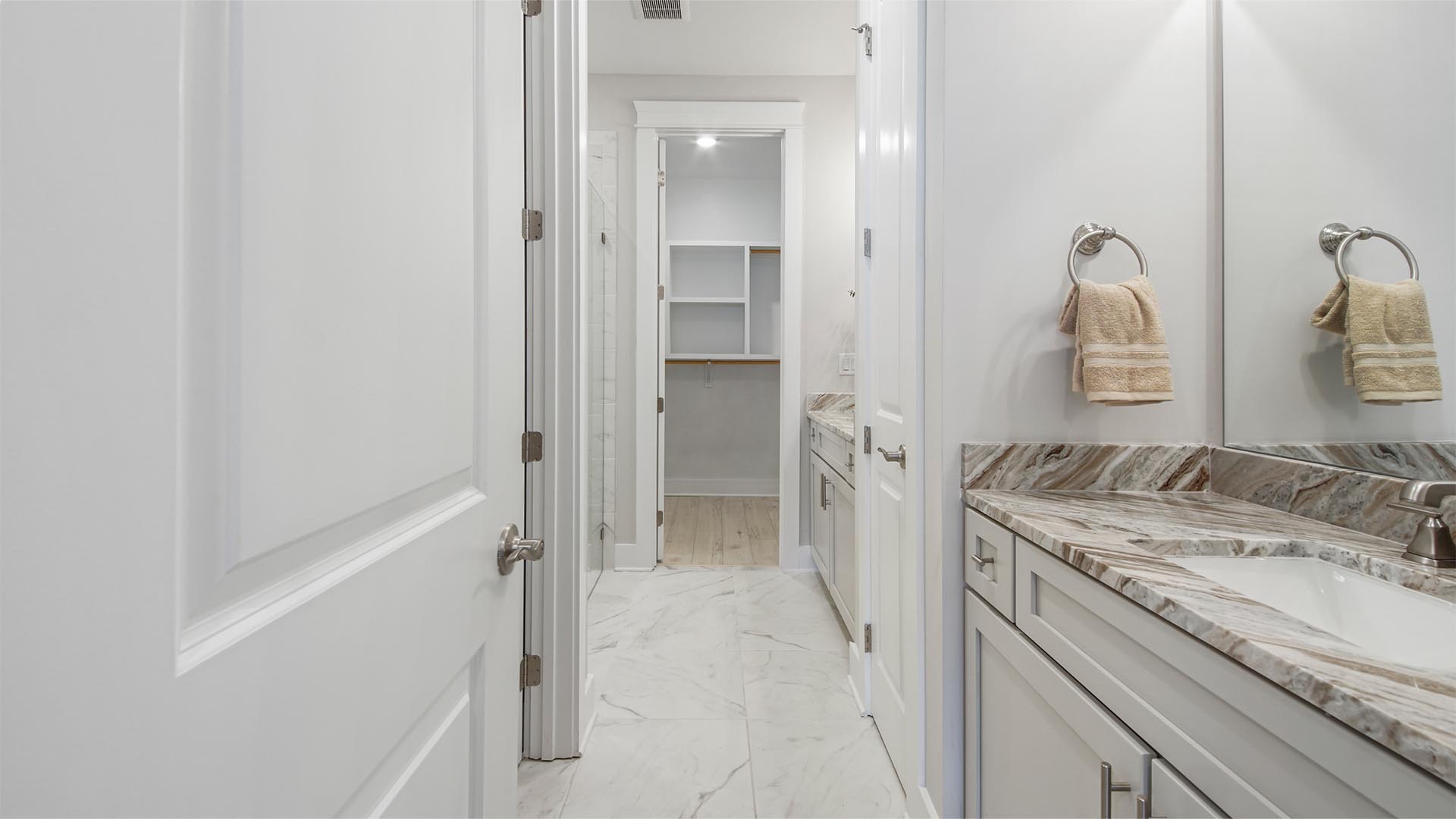 Primary bathroom with tile flooring and two single vanities with quartz countertops and walk-in closet with wood shelving.