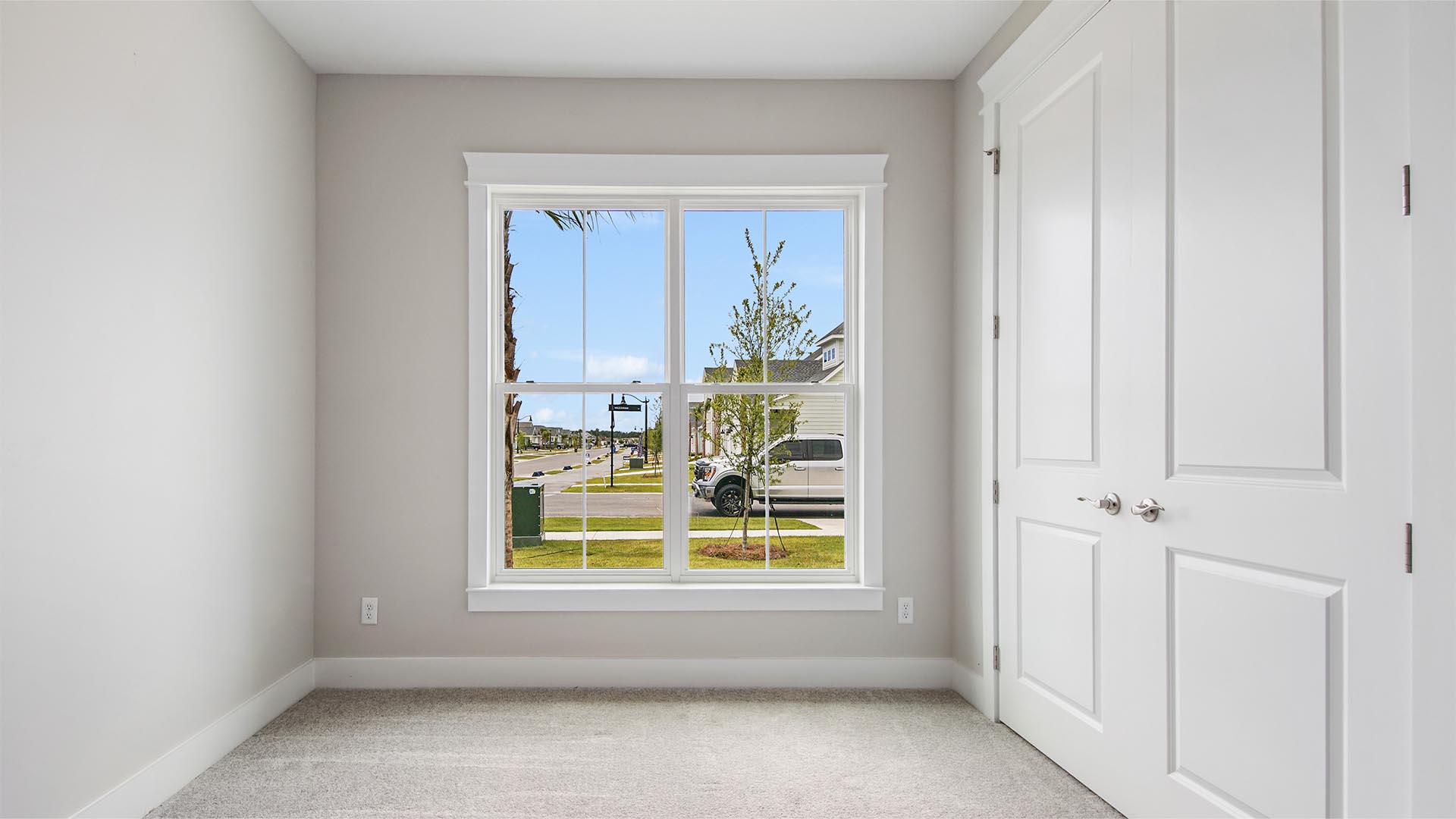Bedroom two with large picture window facing out the front of the home with carpet flooring and double door closet.