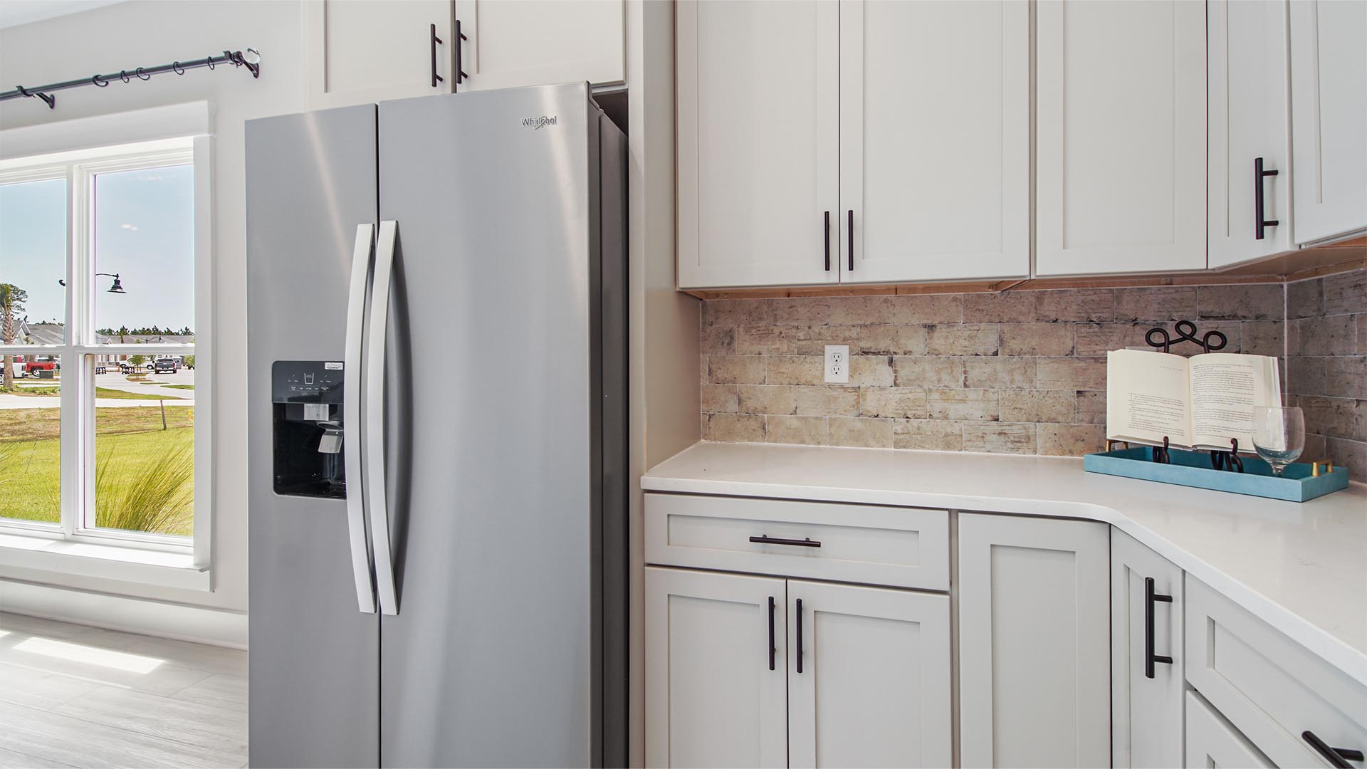 Bright open kitchen with quartz countertops and tile backsplash and a large window and stainless-steel appliances.