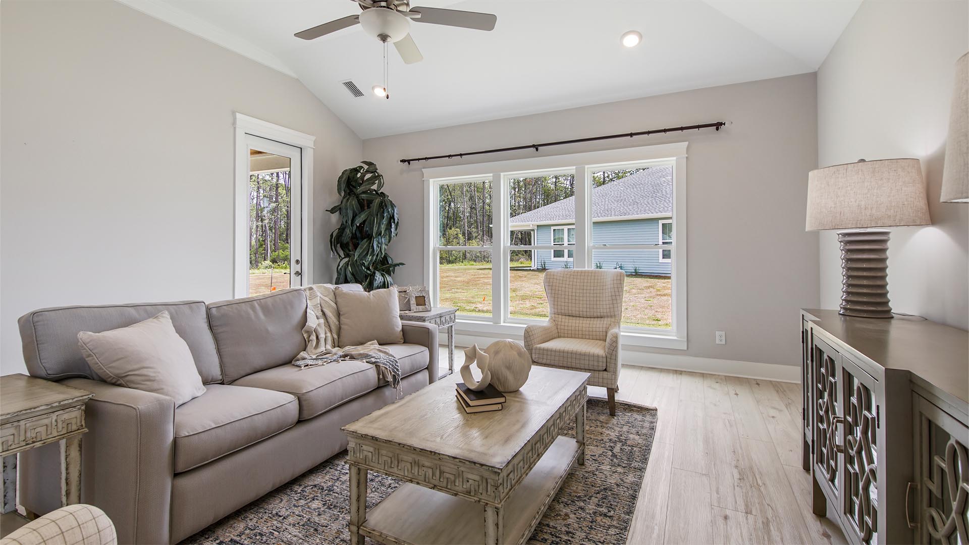Bright living area with large windows and EVP flooring and ceiling fan and hallway to primary bedroom.