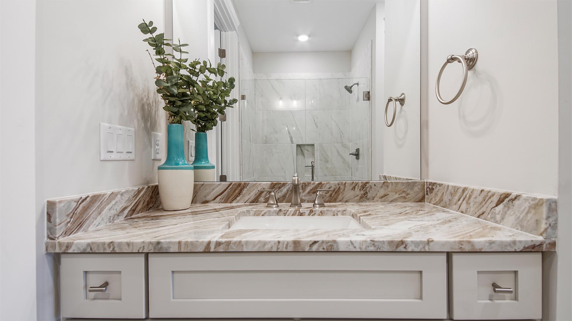 Primary bathroom single vanity with large mirror and quartz countertops and shaker style cabinetry.