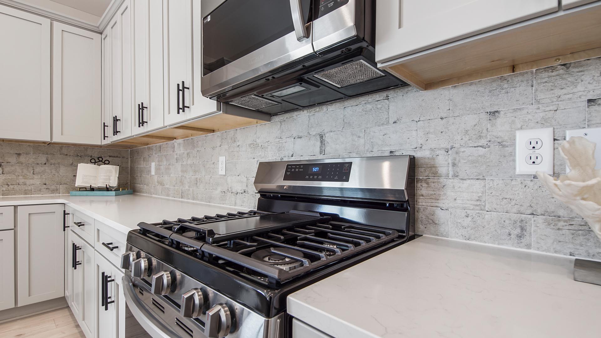 Open kitchen with plenty of storage and gas stove top range and tile backsplash and stainless-steel appliances.