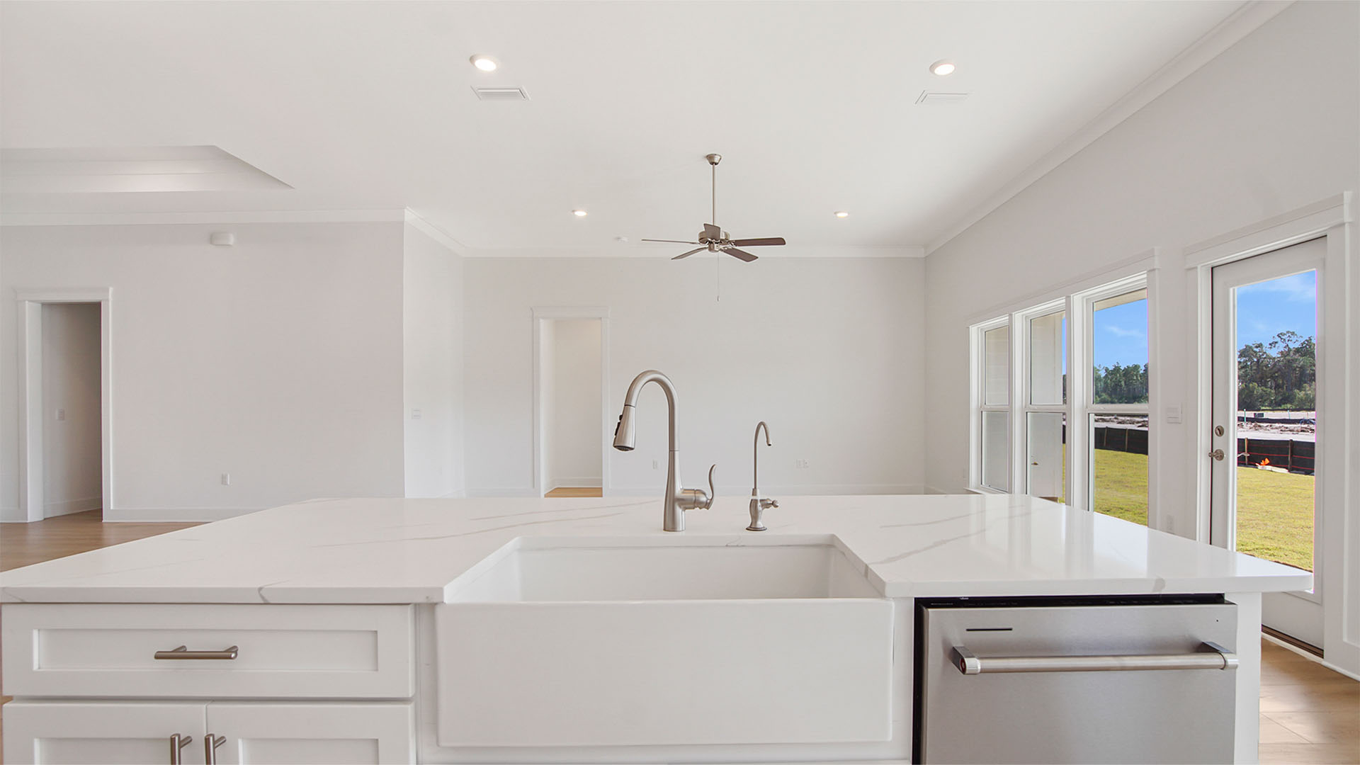 Large kitchen island overlooking living area with well sink and dishwater and quartz countertops and white cabinetry.