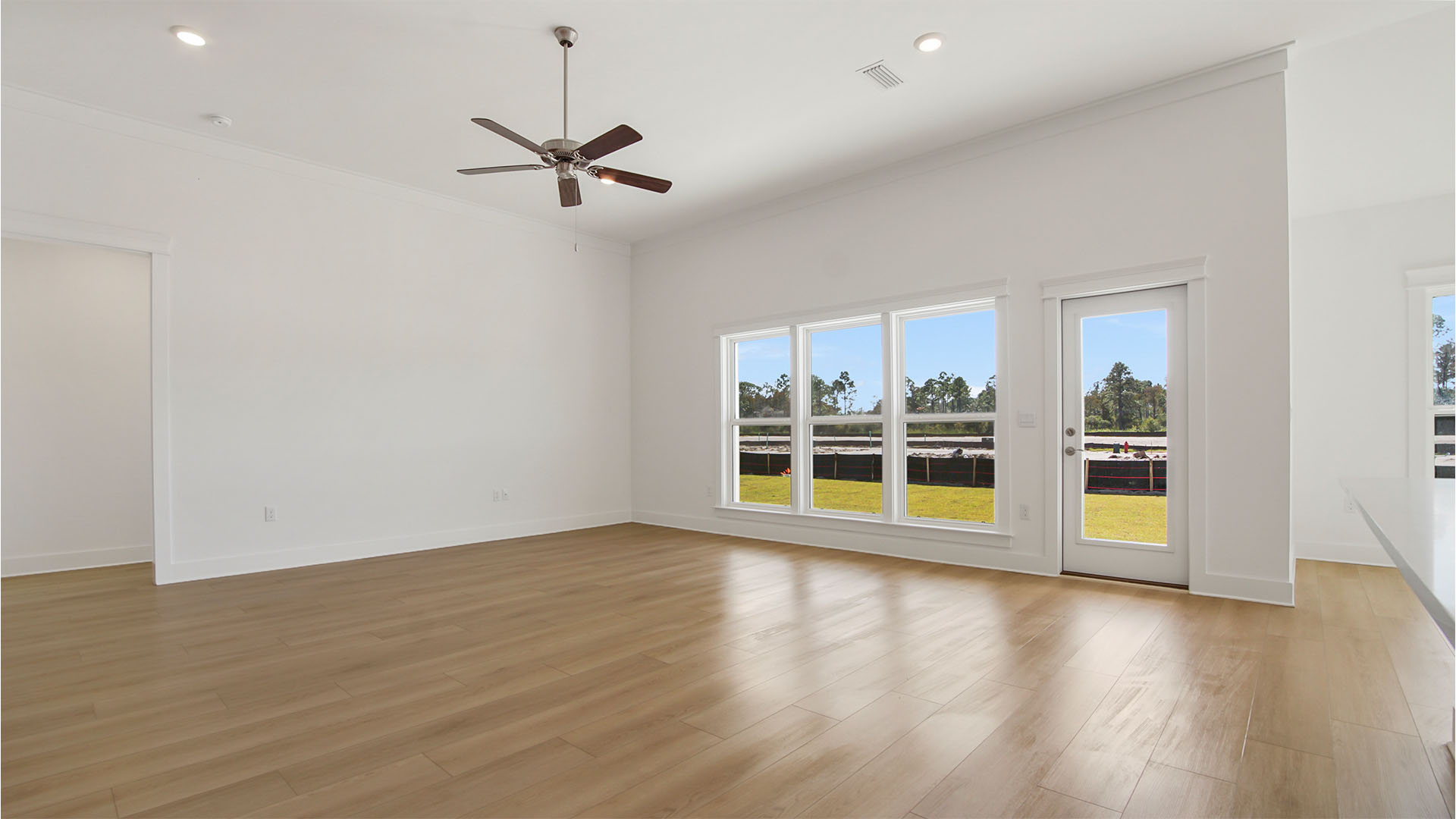 Open living area with large windows and glass back door to cover back patio and tall ceilings and ceiling fan.