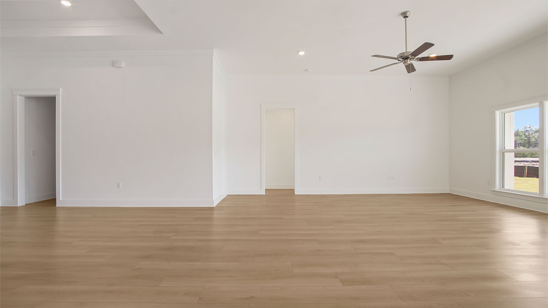 Open living area with EVP flooring and ceiling fan and tall ceilings and hallway to primary bedroom.